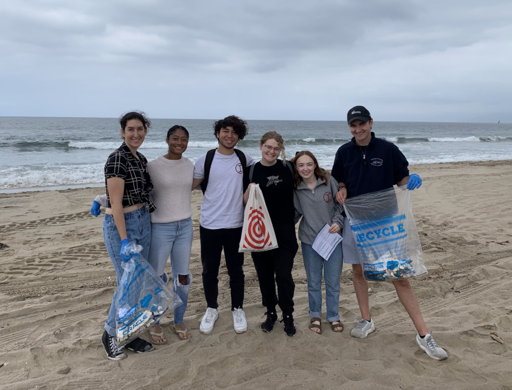 Students stand in the sand at the beach during a beach clean-up.