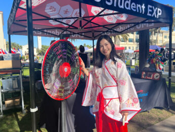 An exchange student stands in front of a prize wheel outside during Wellness Wednesday.