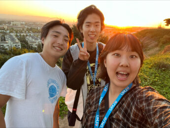 Three Asian students pose outside on the bluff during a sunset sky.