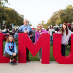 A family and their LMU student pose in front of the red LMU letters.