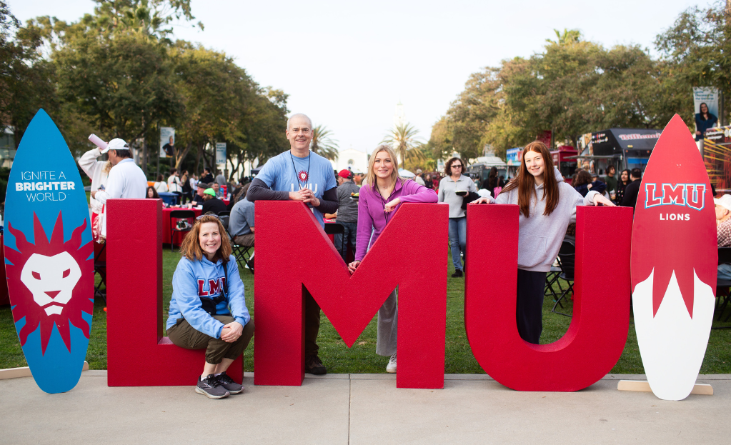 A family and their LMU student pose in front of the red LMU letters.