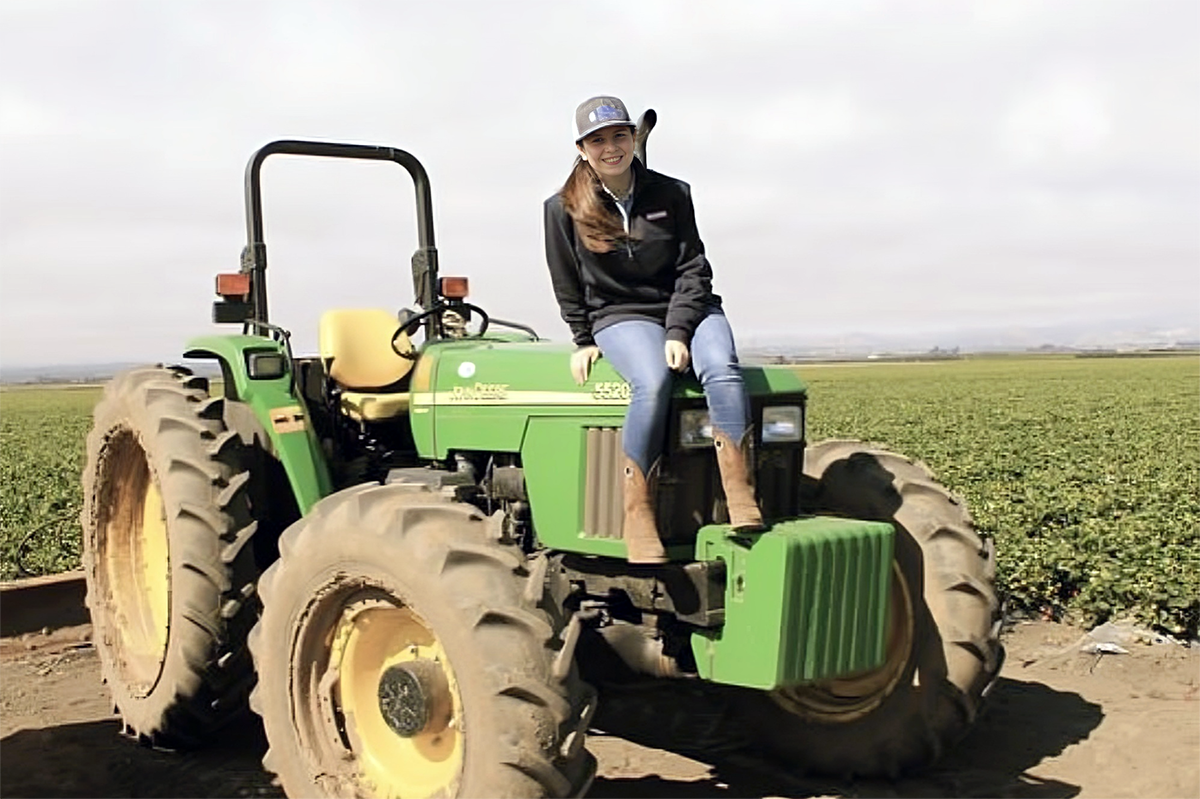 A young woman sits on a tractor in a field
