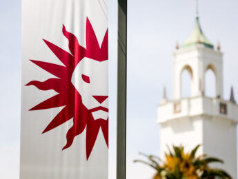 A white flag with the red LMU Spirit Mark and the clock tower in the background.
