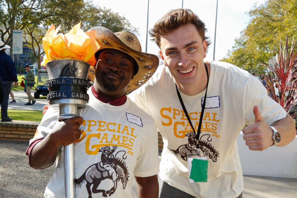 A Special Games athlete holding the torch and student volunteer pose in light yellow shirts outside.