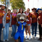 Students in brown shirts and Wester hats pose with the Rams mascot in a blue football uniform.