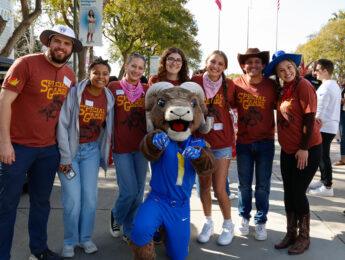 Students in brown shirts and Wester hats pose with the Rams mascot in a blue football uniform.