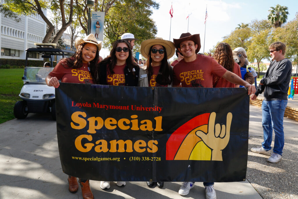 Students and staff in brown shirts and Western-themed hats hold up a black banner for Special Games.