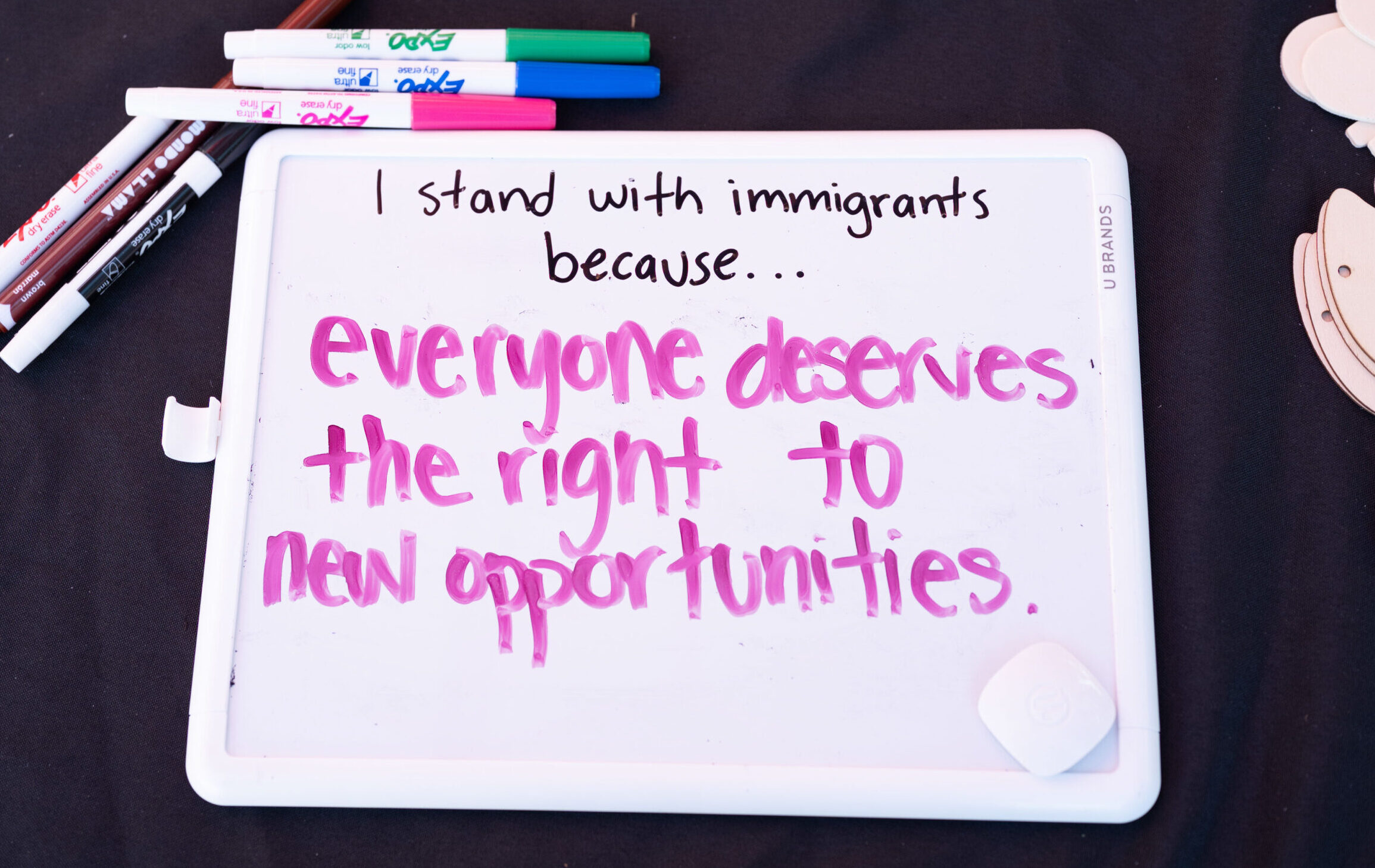 A dry erase board with pink marker reads "I stand with immigrants because...everyone deserves the tight to new opportunities."