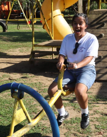 A student in a white t-shirt and jeans bounces on yellow playground equipment.