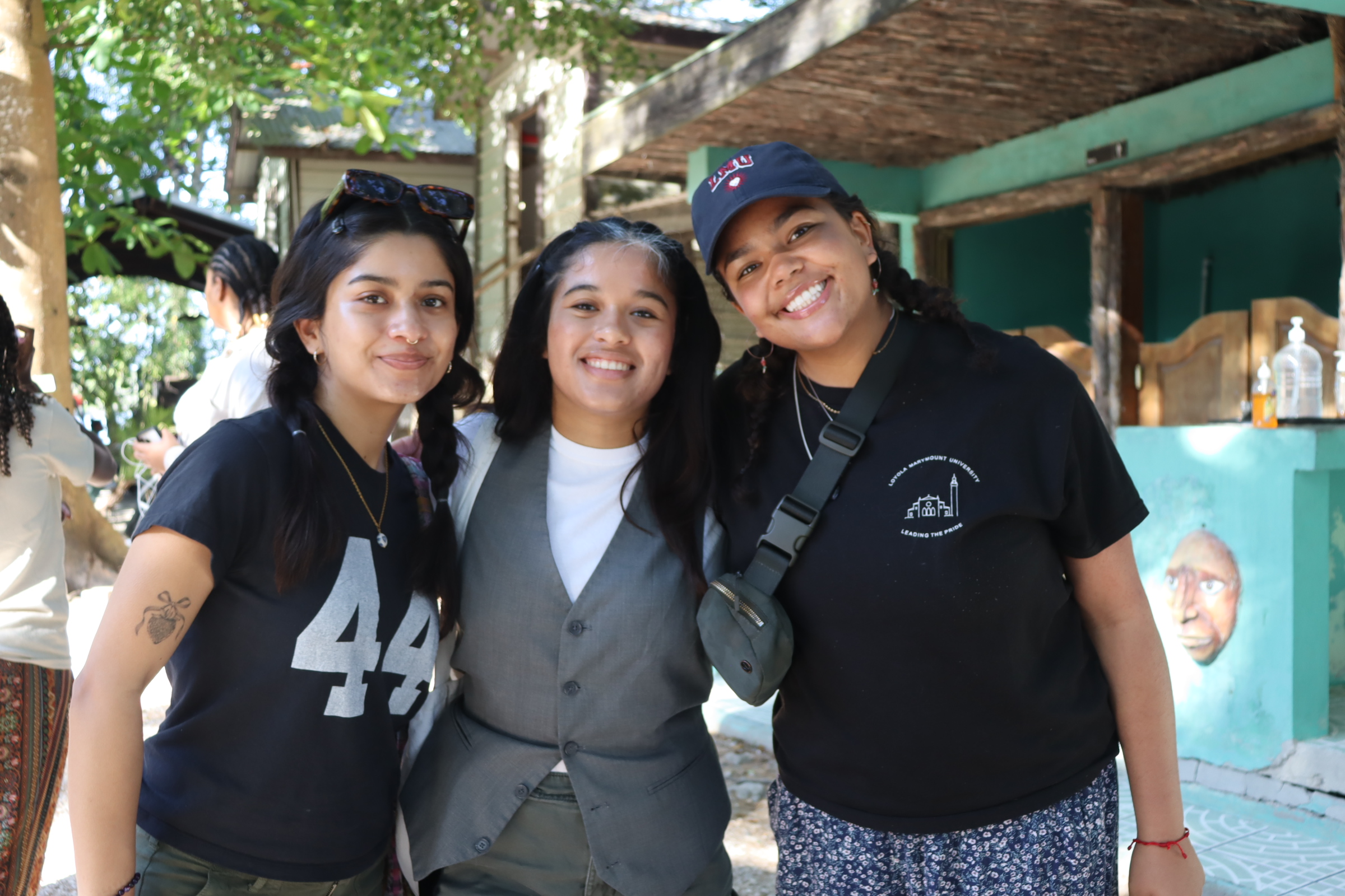 Three female students in black shirts and a grey shirt and vest pose outside.