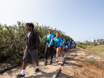 Students and a volunteer walk outside on a dirt path.